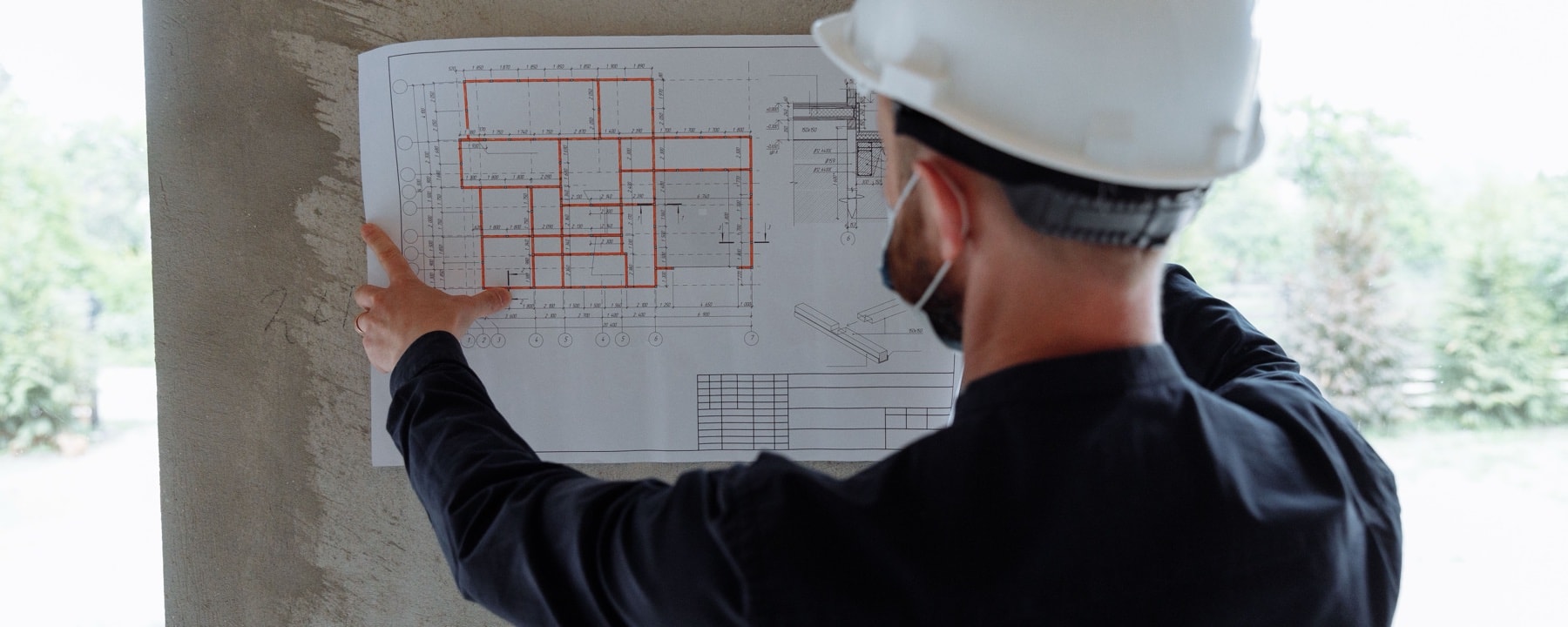 Persona con casco señalando un plano de obra apoyado sobre una columna de hormigón.